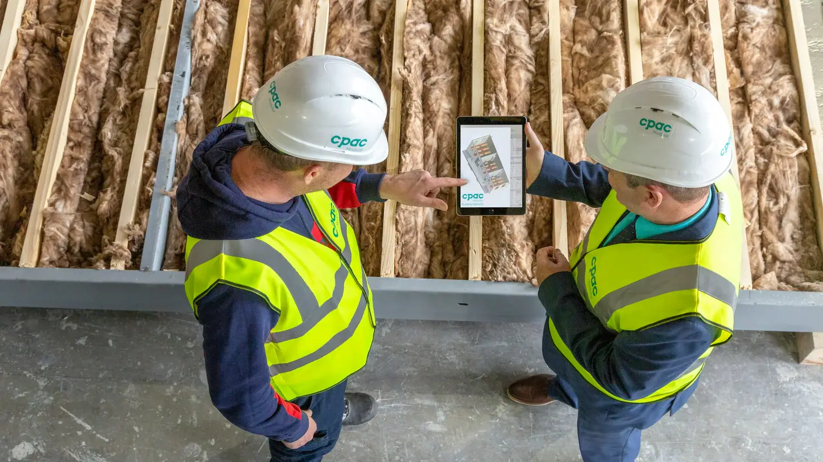 Deux professionnels du bâtiment consultent un plan sur une tablette, sur un chantier.
