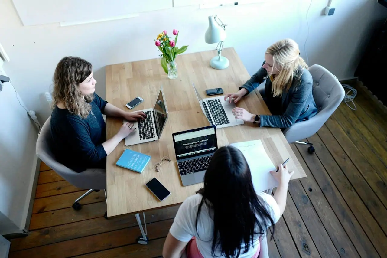 Trois personnes en atelier autour d'une table de travail, ordinateurs ouverts