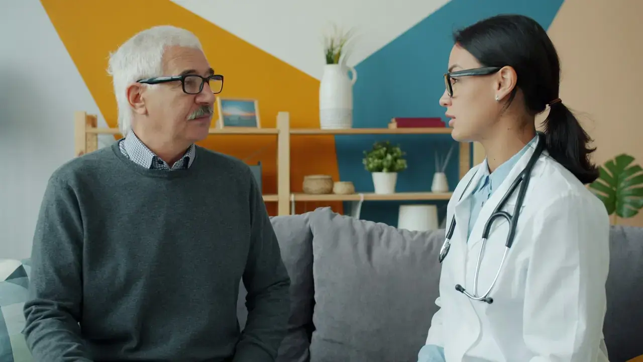 Une professionnelle en blouse échange avec un résident âgé, dans un salon d’établissement.