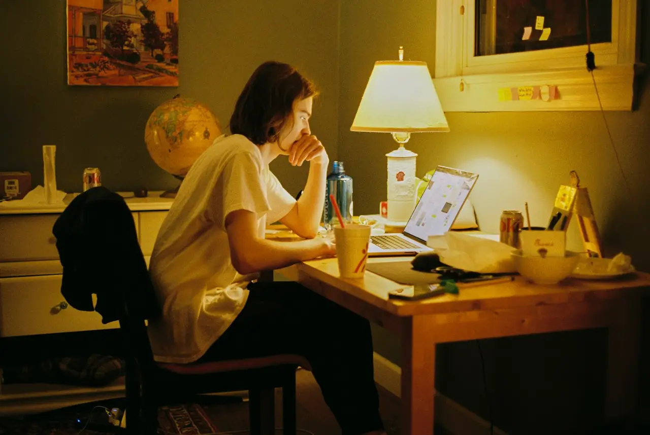 Une femme travaille tard le soir sur son ordinateur, sous la lampe de son bureau.