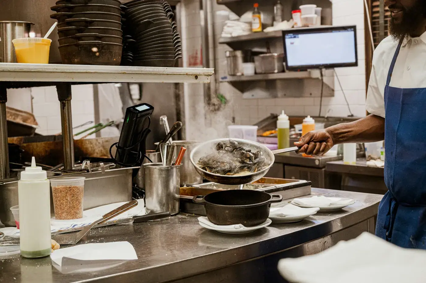 Un cuisinier dresse une assiette à côté de l'écran de commandes, en plein service.