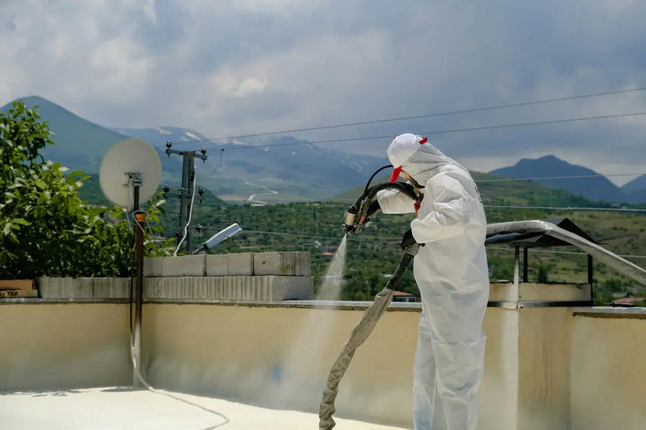 Photo d’illustration : un étancheur projette un revêtement d’étanchéité sur une toiture-terrasse, montagnes en arrière-plan.
